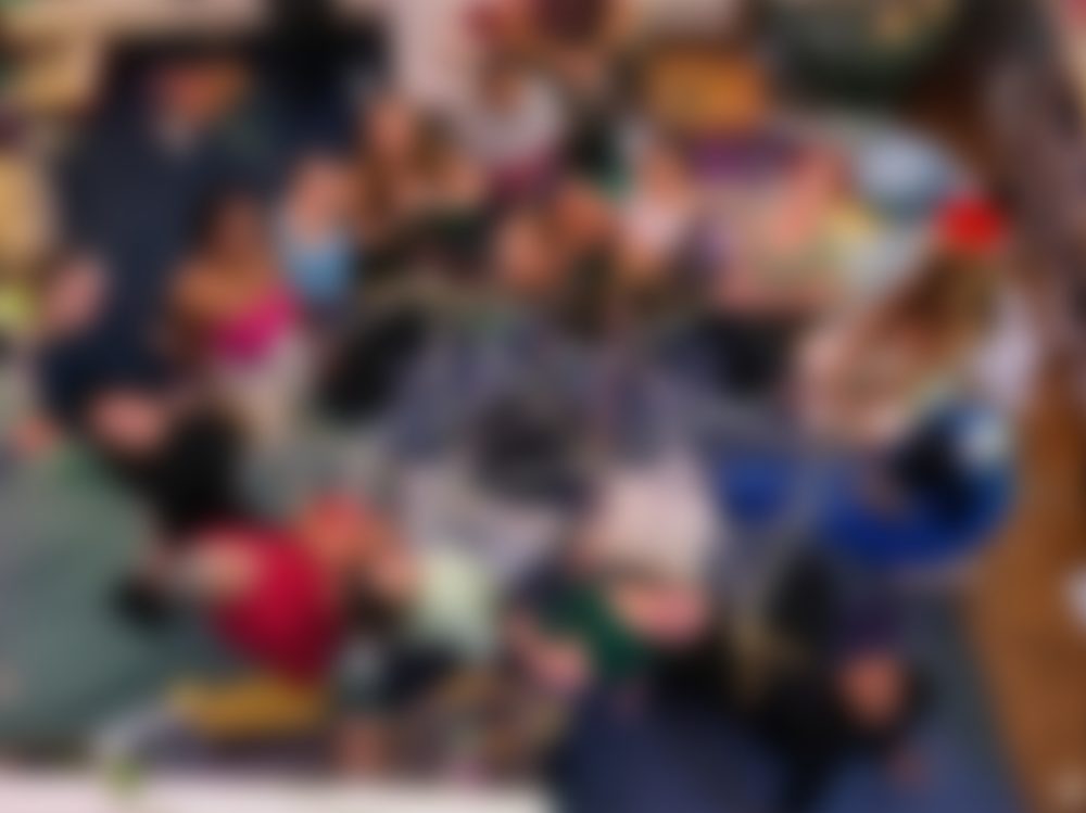 A blurred photo of a gathering seated in a circle on the floor.